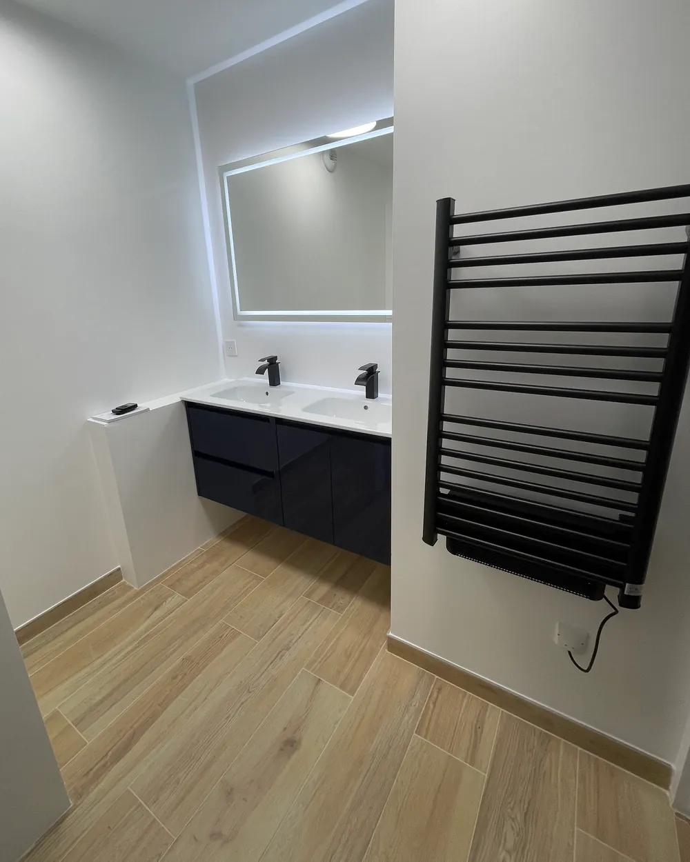 Salle de bain rénovée : double vasque, miroir lumineux et sèche-serviettes noir